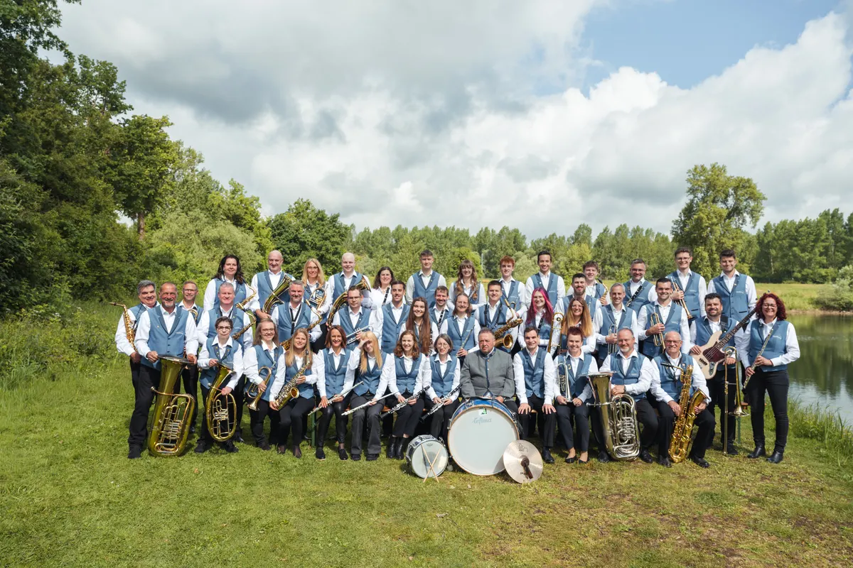 Großes Gruppenfoto des Musikvereins mit allen Instrumenten, darunter Pauke und Tuba, am Seeufer.